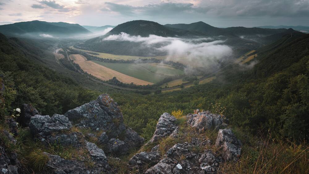 Une vallée traversée par une route sinueuse, entourée de montagnes et de champs.