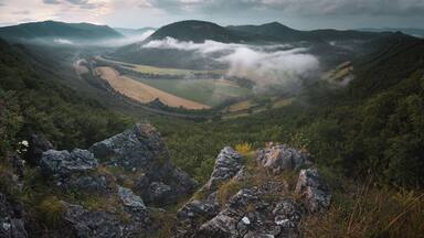 Un valle con un camino serpenteante, rodeado de montañas y campos.