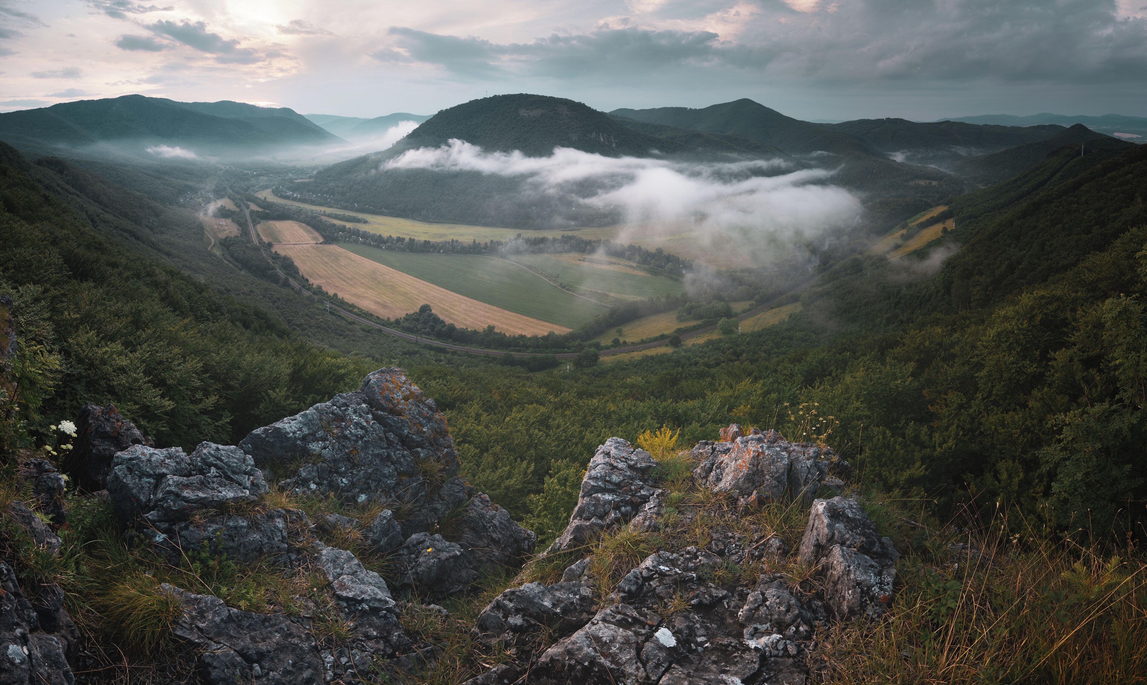 A valley with a winding road, surrounded by mountains and fields.