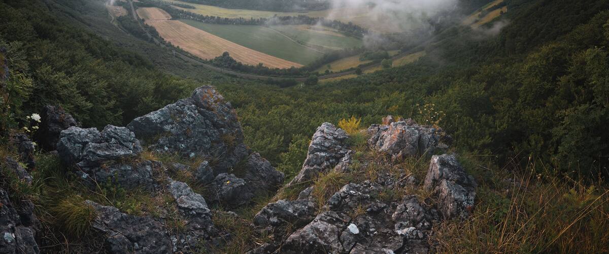 A valley with a winding road, surrounded by mountains and fields.