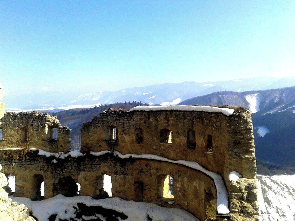A snow-covered ruin with multiple arches and a mountainous backdrop.