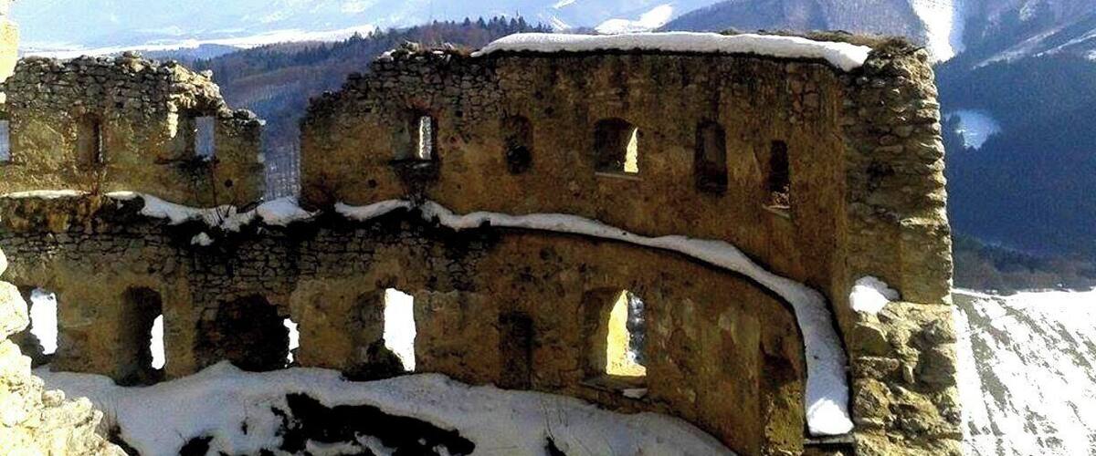 A snow-covered ruin with multiple arches and a mountainous backdrop.