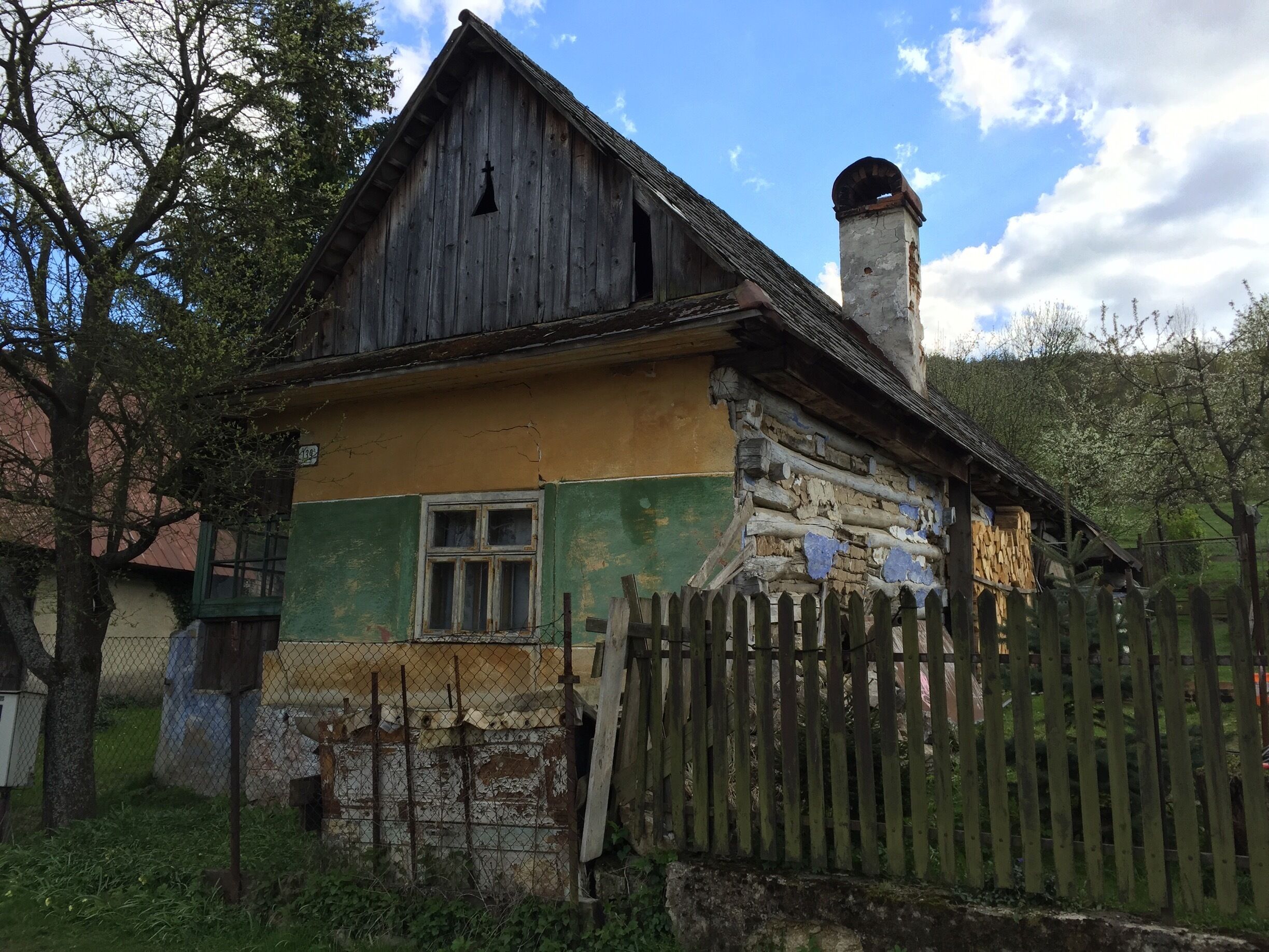 A rustic wooden house with a green and yellow facade, a chimney, and a wooden fence.