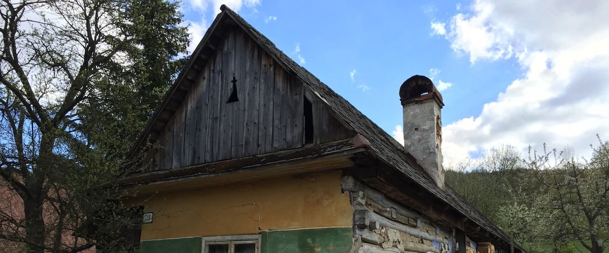 A rustic wooden house with a green and yellow facade, a chimney, and a wooden fence.