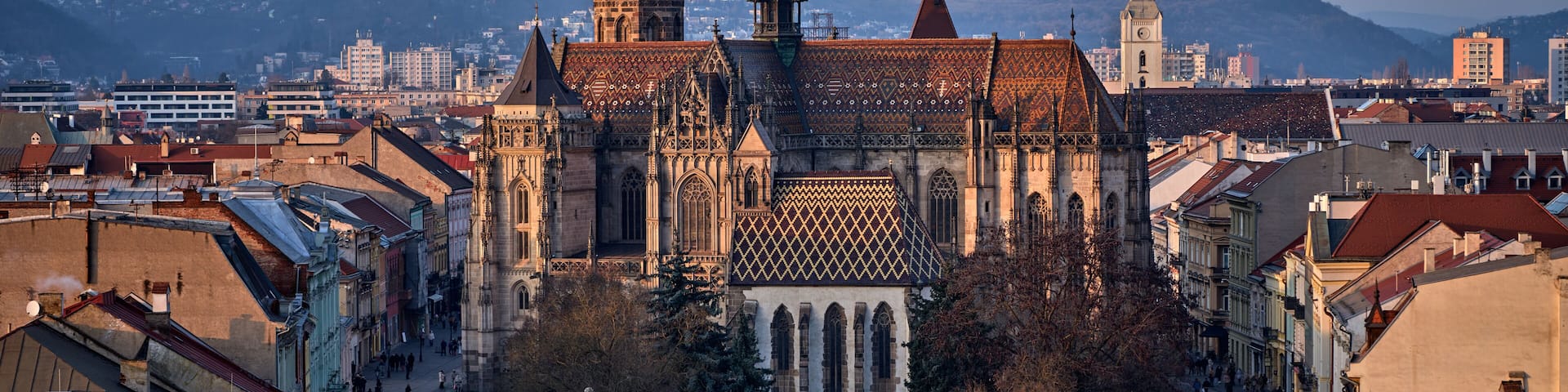 A historic cathedral with intricate architecture, a central square with a fountain, and surrounding urban buildings.