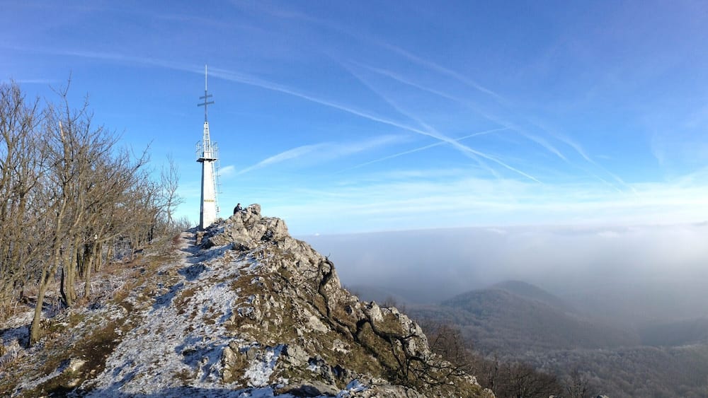 Une croix sur le sommet rocheux d’une colline, d’où l’on peut admirer une vallée et des montagnes lointaines.