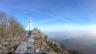 Una cruz en la cima rocosa de una colina, con vistas a un valle y montañas distantes.