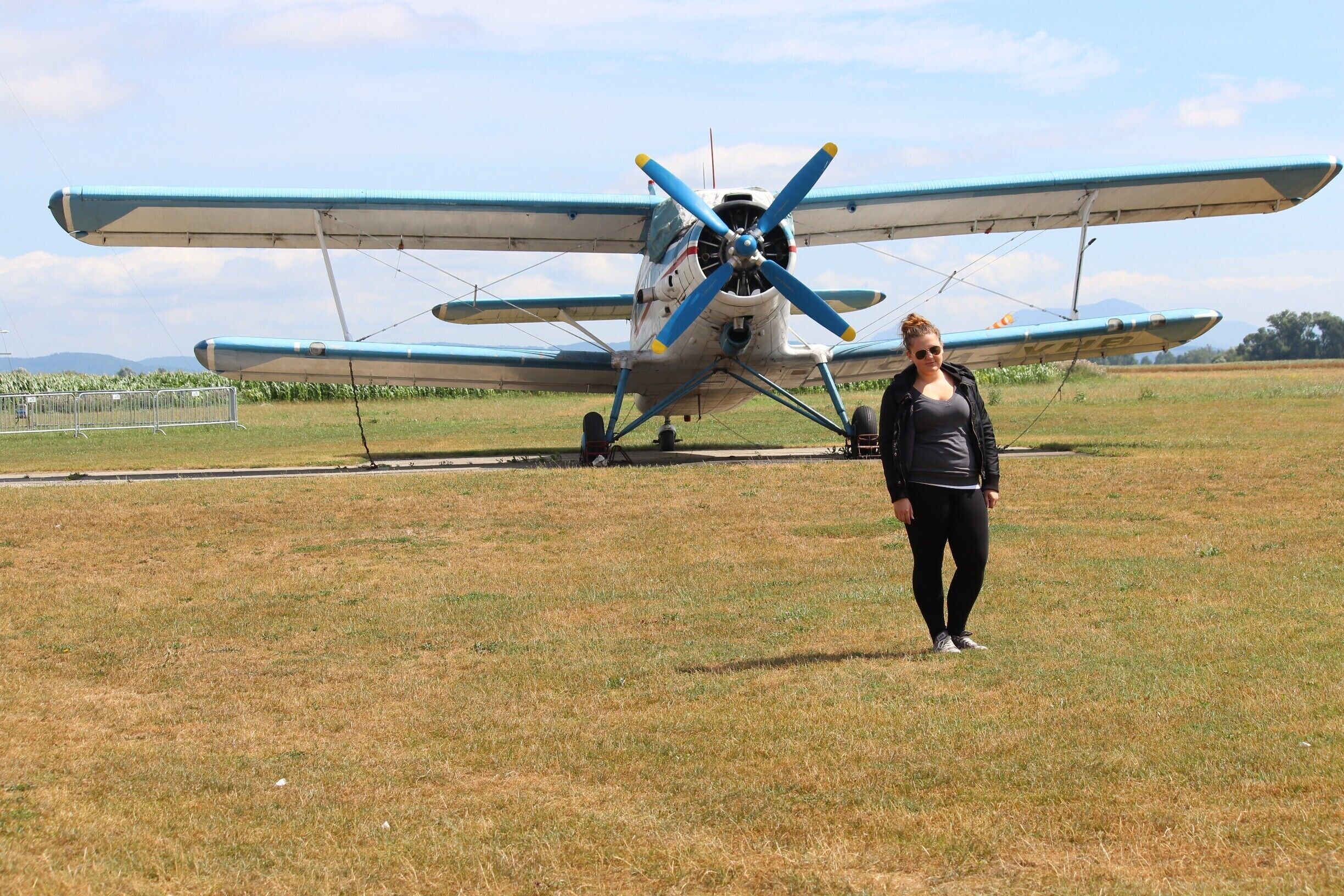 A vintage blue and white biplane on a grassy field with mountains in the background.