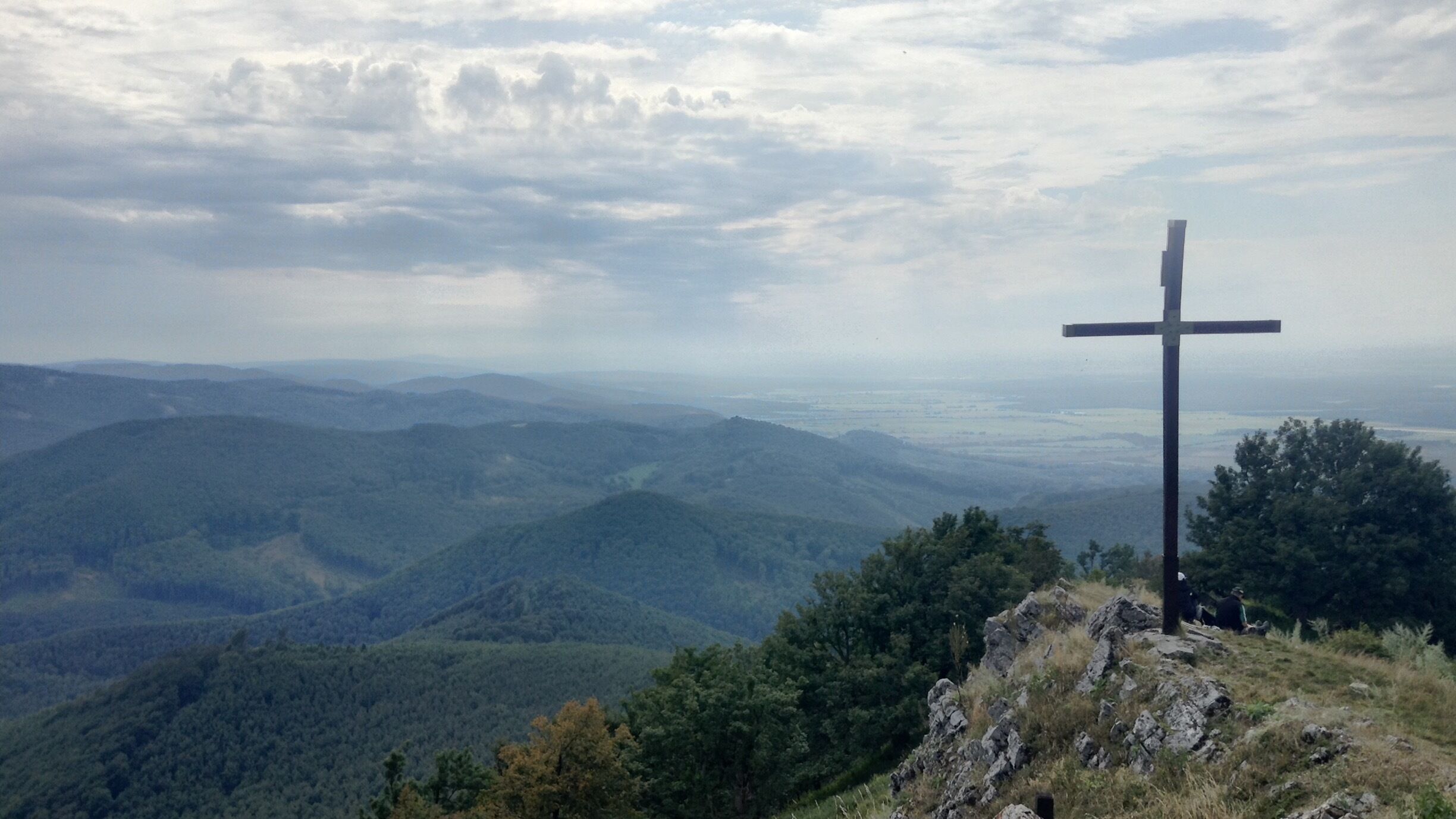 A cross on a hill overlooking a forested valley.