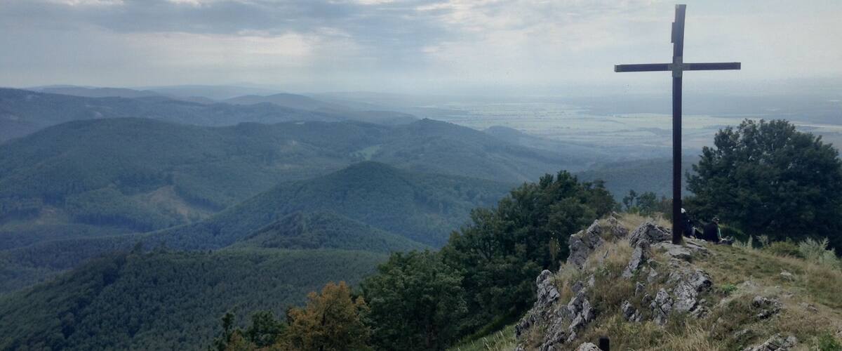 A cross on a hill overlooking a forested valley.