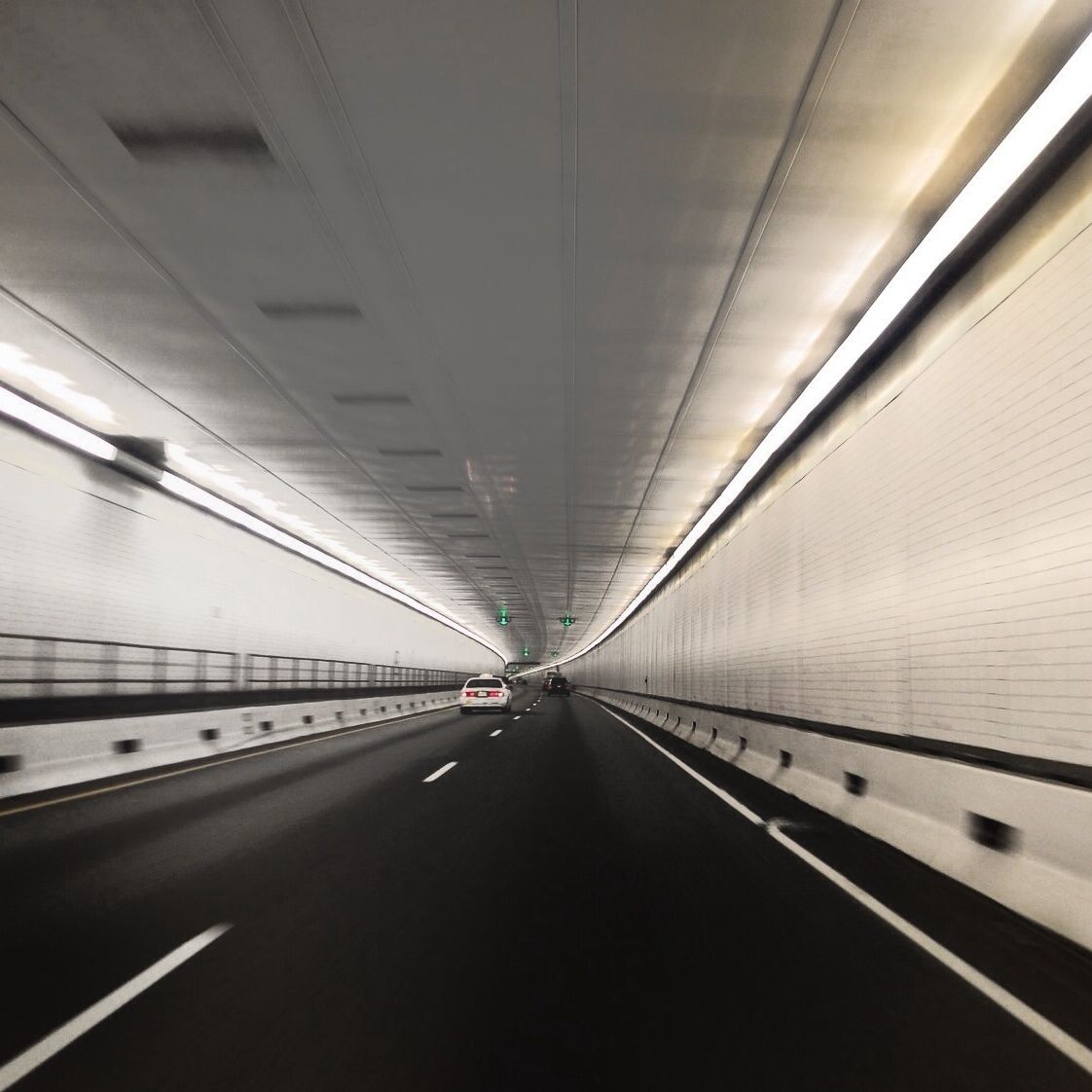 A tunnel with a road, white walls, and overhead lighting.