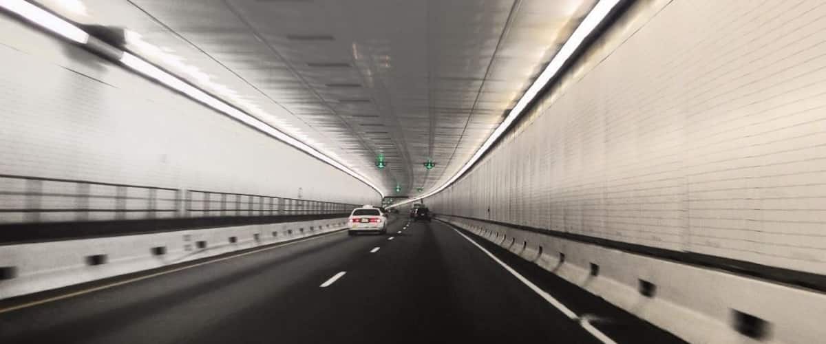 A tunnel with a road, white walls, and overhead lighting.