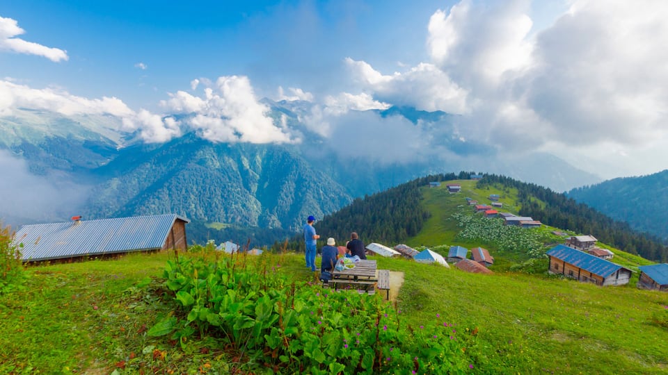 A mountainous landscape with a clear sky, a wooden bench, and several small buildings.