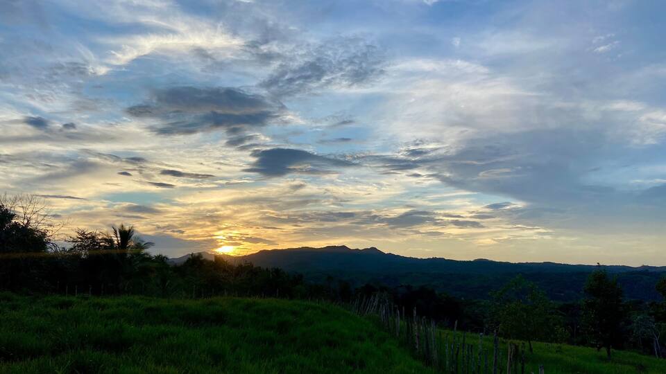 A sunset over a grassy hill with a mountain range in the distance.
