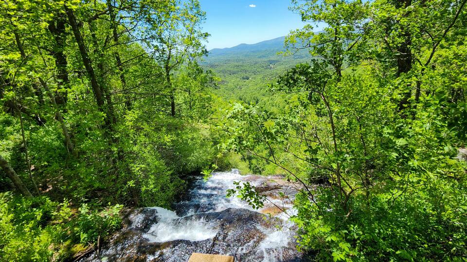 A waterfall surrounded by dense green forest and distant mountains.