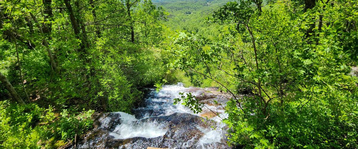 A waterfall surrounded by dense green forest and distant mountains.