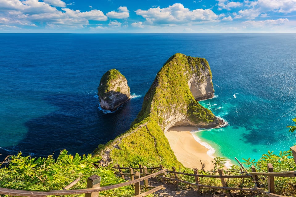 A coastal landscape with a prominent rock formation, a sandy beach, and a clear blue sea.