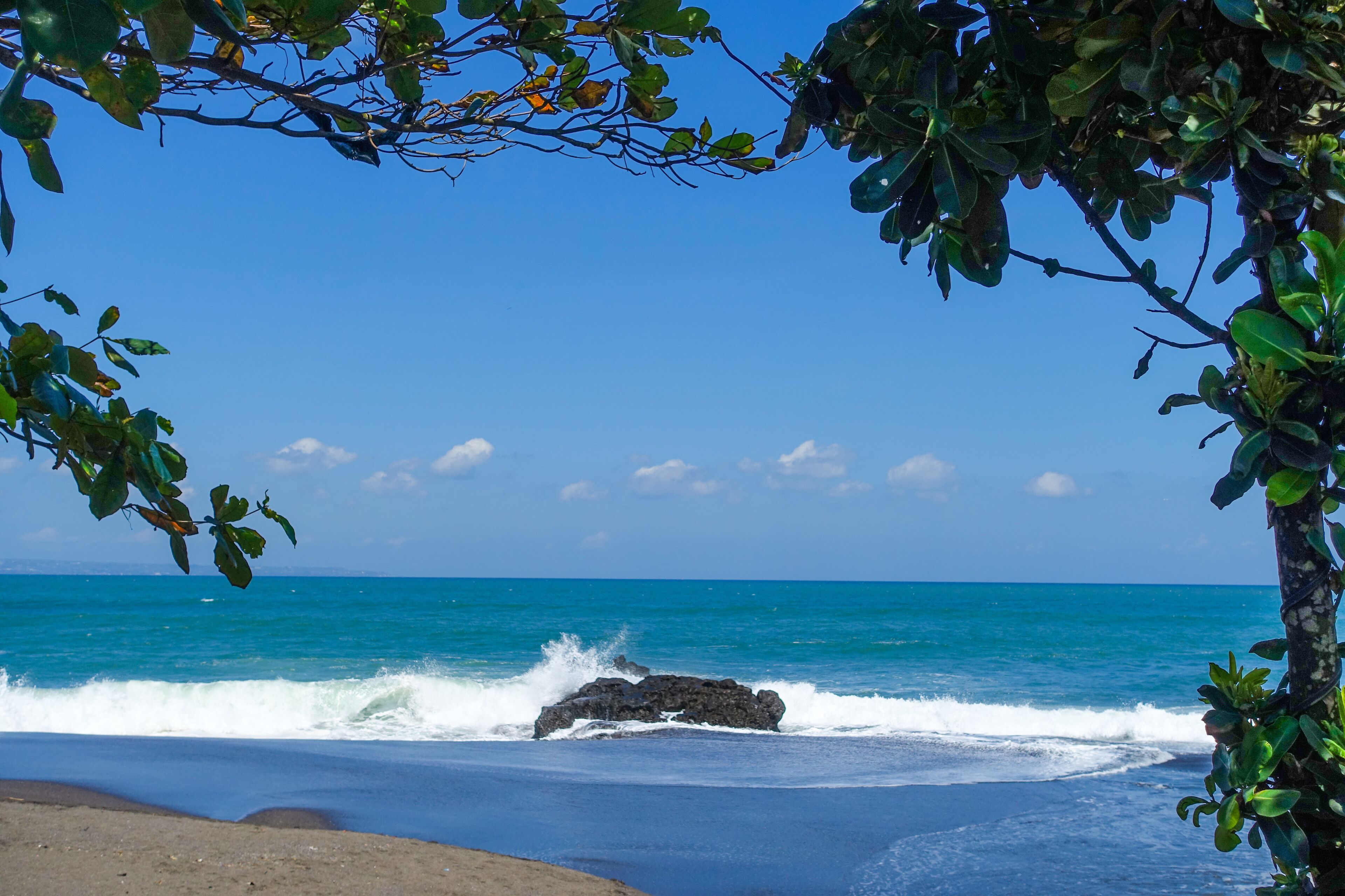A beach with waves crashing against rocks and a clear blue sky.