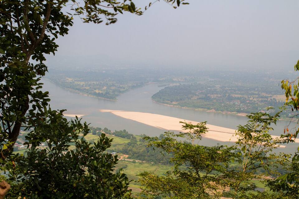 A river winding through a valley with surrounding greenery and distant buildings.