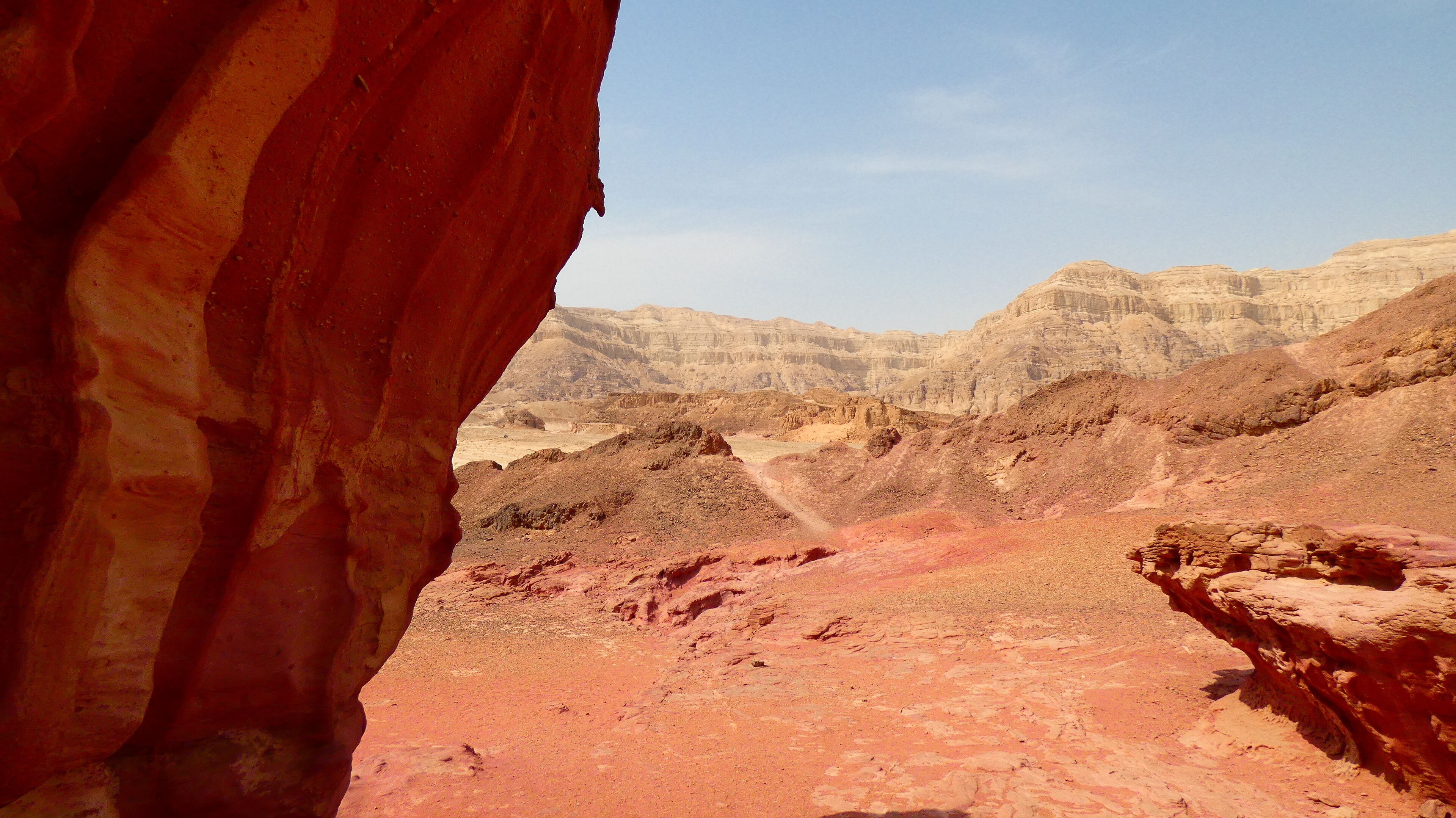 Formación rocosa roja con vistas a acantilados sedimentarios estratificados al fondo.