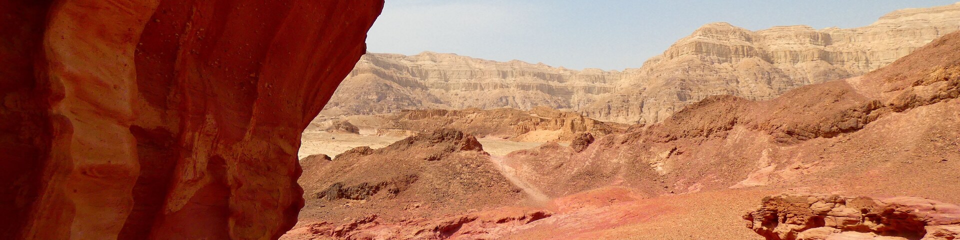 Formación rocosa roja con vistas a acantilados sedimentarios estratificados al fondo.