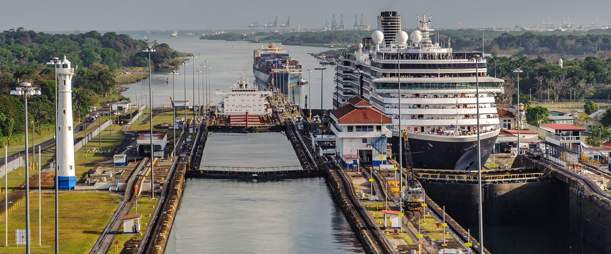 Ein großes Kreuzfahrtschiff liegt im Hafen, im Hintergrund steht ein Leuchtturm.