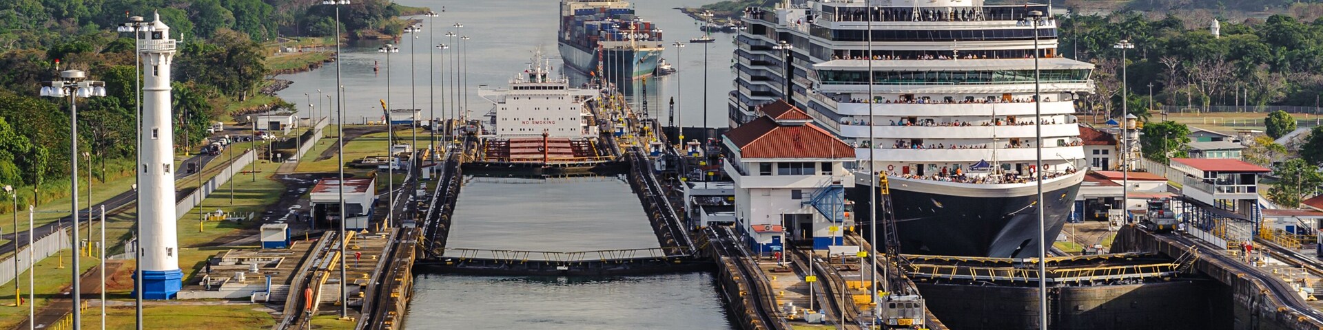 Um grande navio de cruzeiro atracado num porto, com um farol ao fundo.