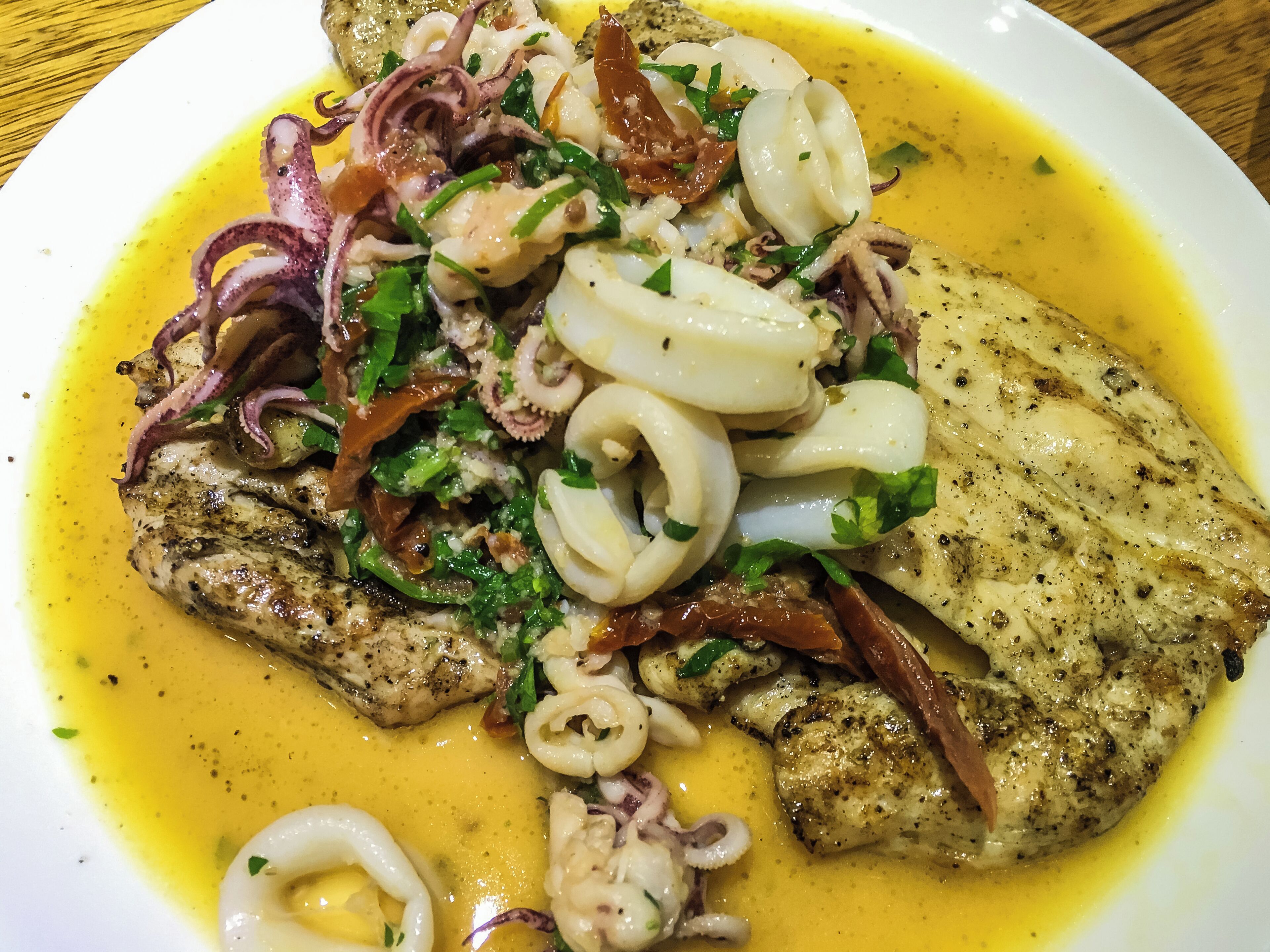 A plate of grilled fish with squid rings, onions, and herbs.