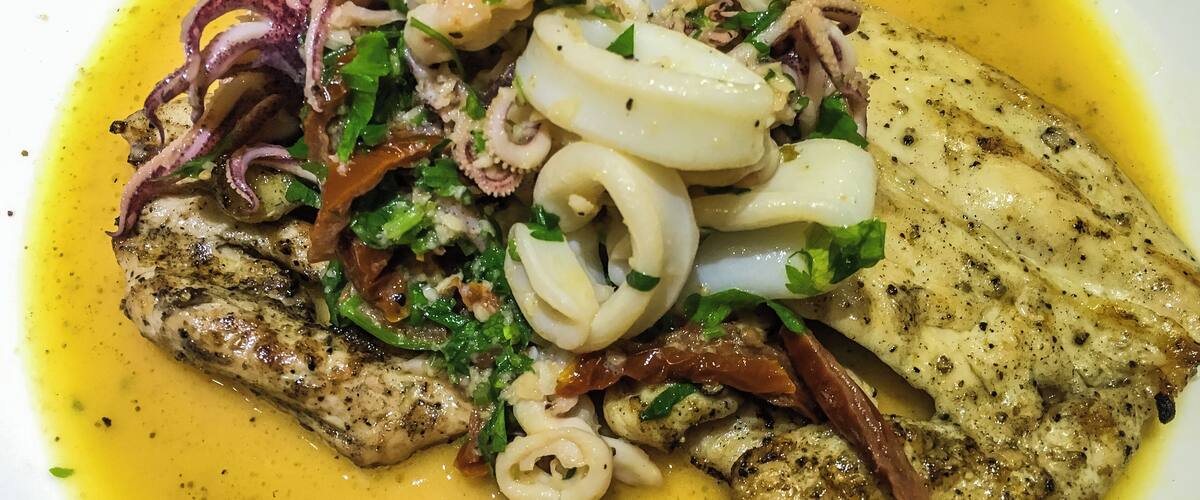 A plate of grilled fish with squid rings, onions, and herbs.