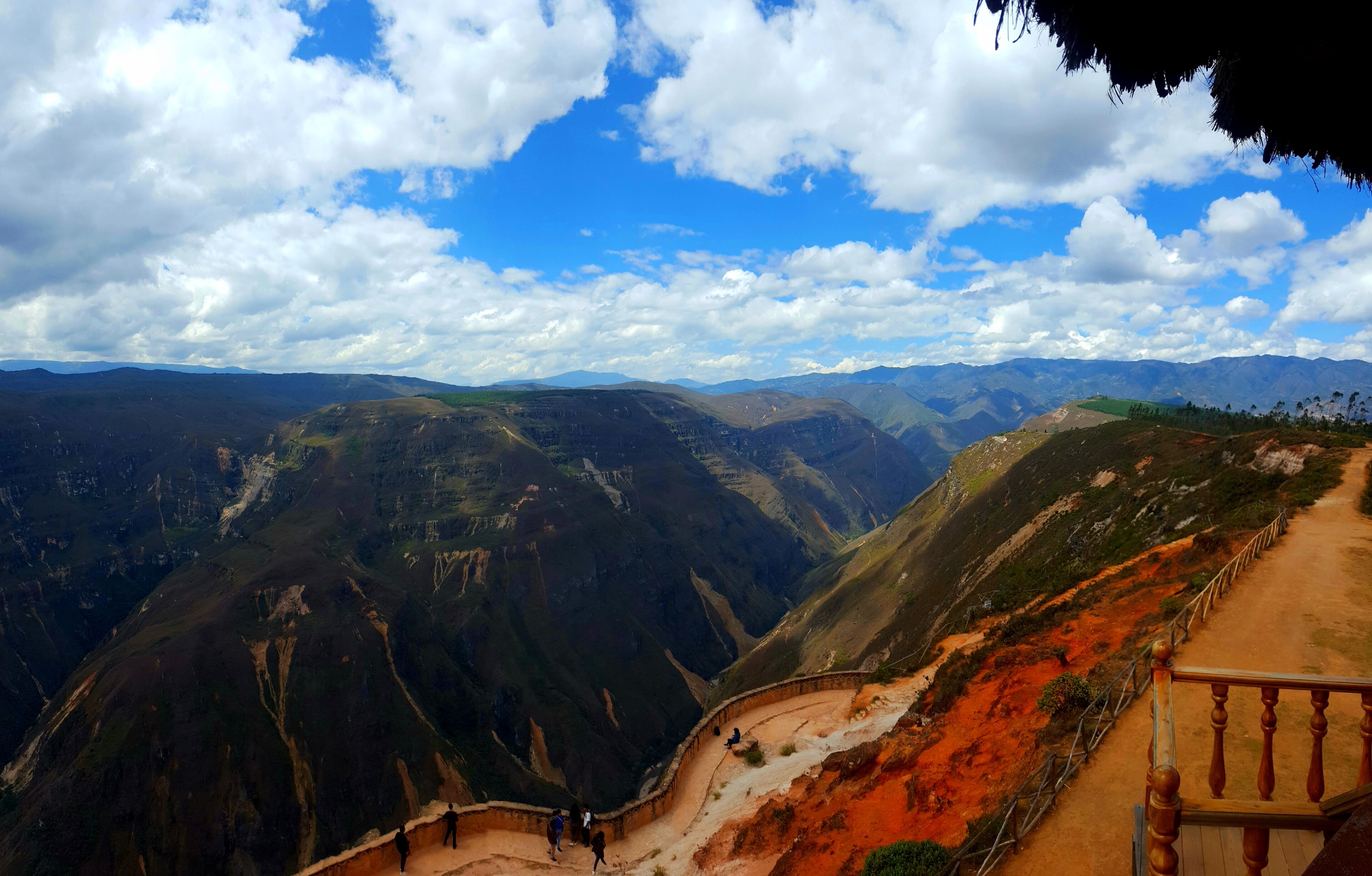 A mountainous landscape with a dirt path and wooden railing.