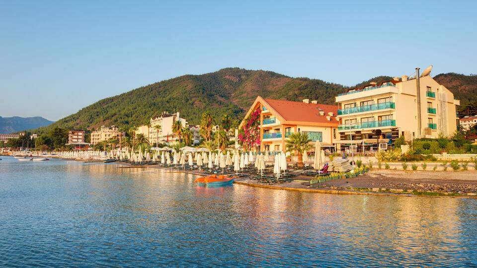 A waterfront with a boat, buildings, and a hill in the background.