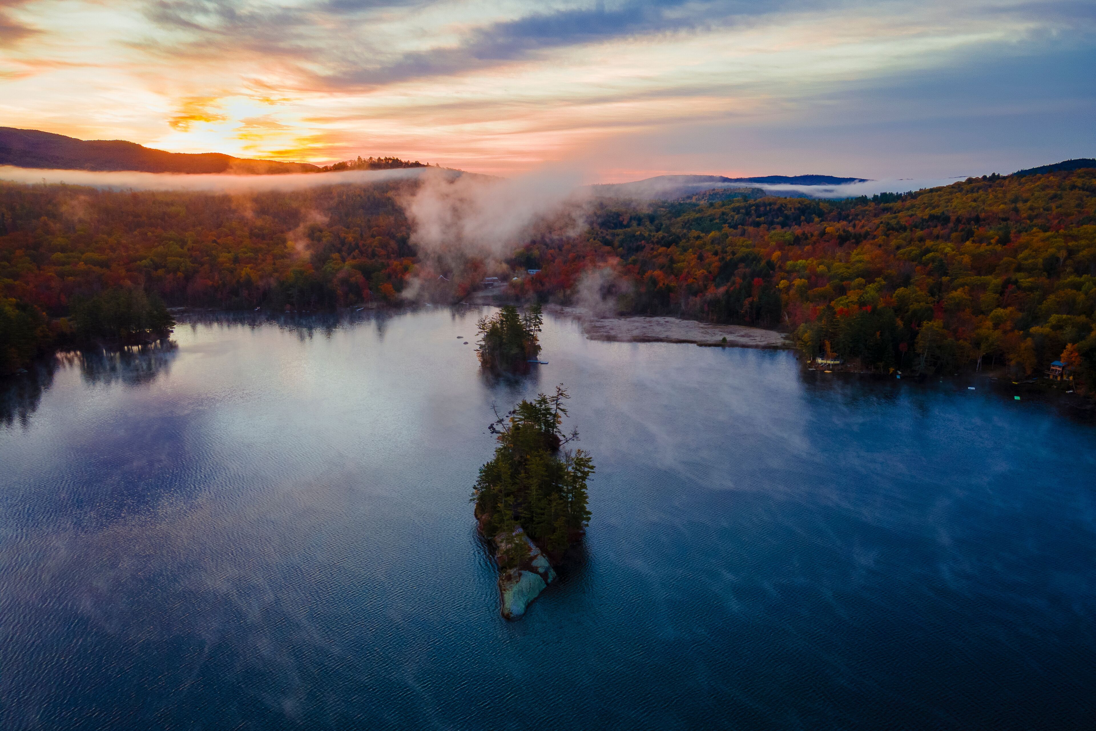 Aerial view of a serene and picturesque lake with an island surrounded by colorful autumn foliage and misty trees, Bryant Pond, United States.