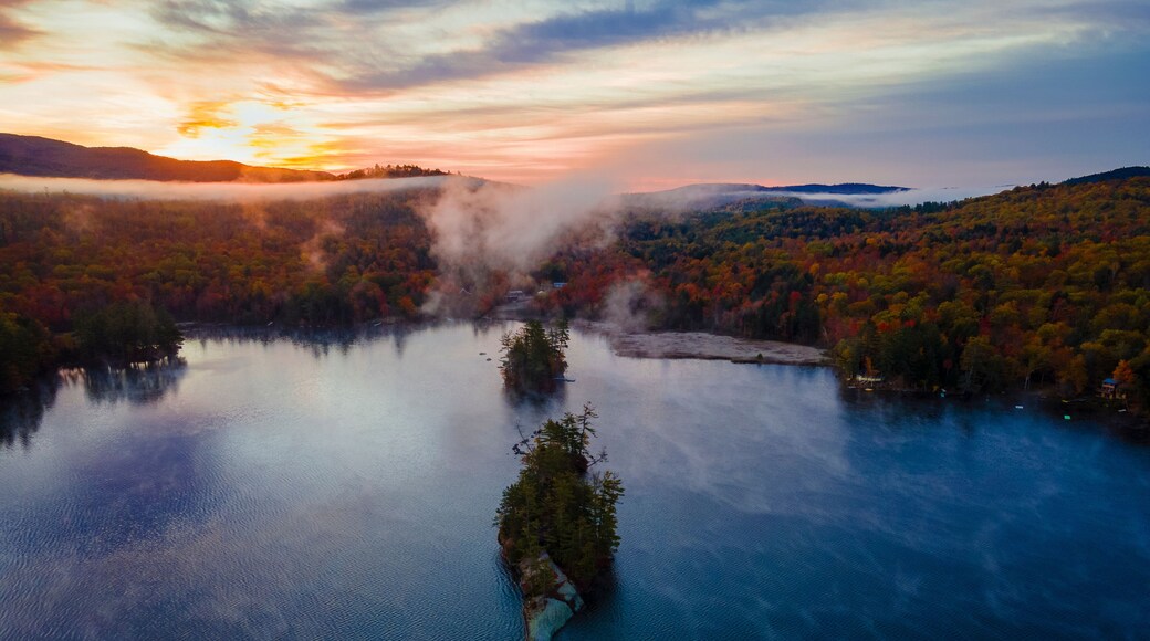 Aerial view of a serene and picturesque lake with an island surrounded by colorful autumn foliage and misty trees, Bryant Pond, United States.