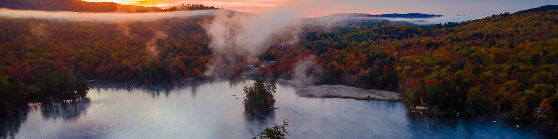 Aerial view of a serene and picturesque lake with an island surrounded by colorful autumn foliage and misty trees, Bryant Pond, United States.