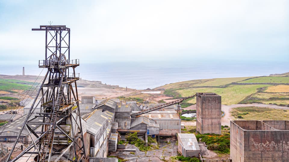 An industrial area with a conveyor belt system, large metal structures, and a coastal landscape in the background.