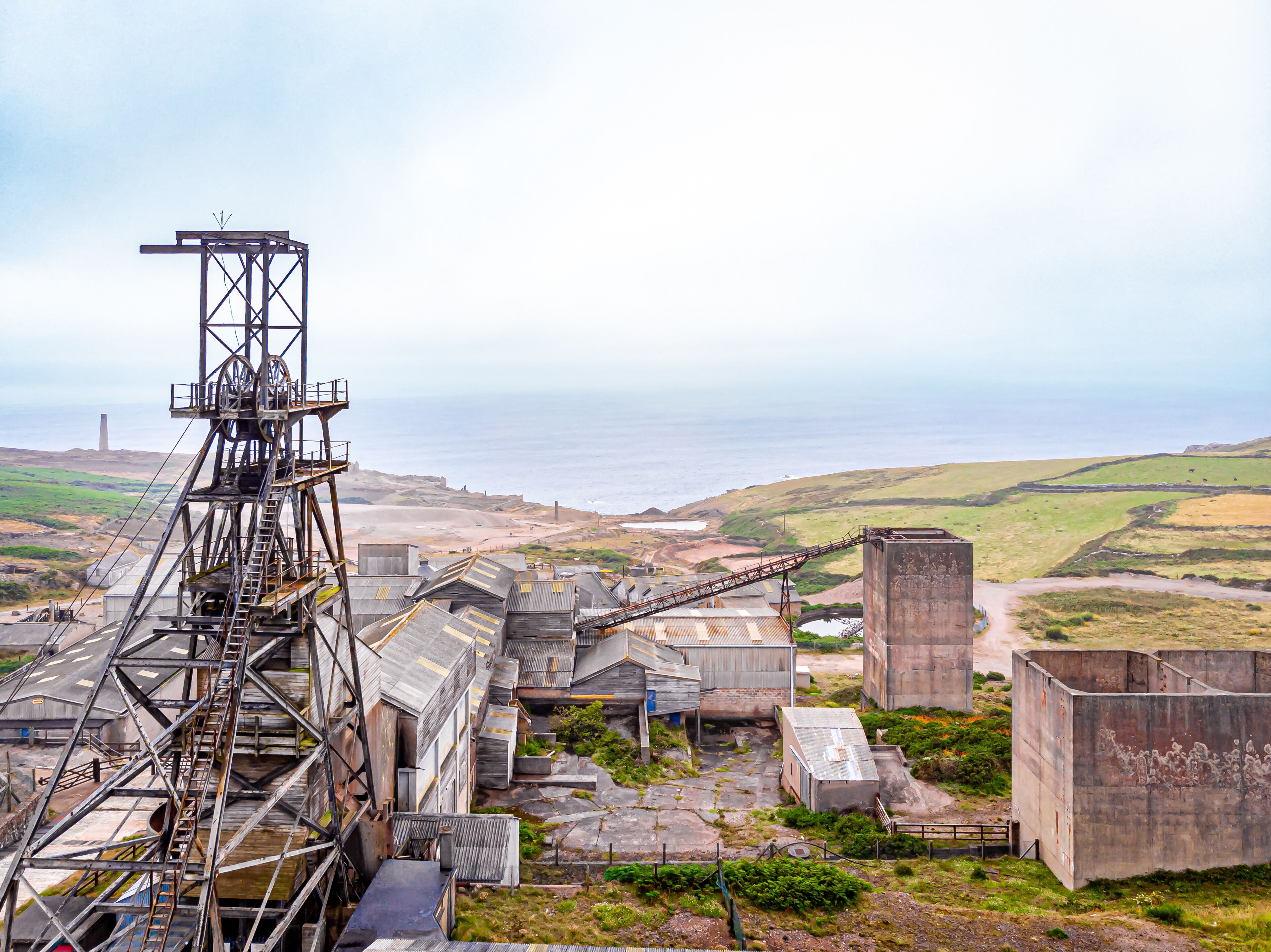 An industrial area with a conveyor belt system, large metal structures, and a coastal landscape in the background.