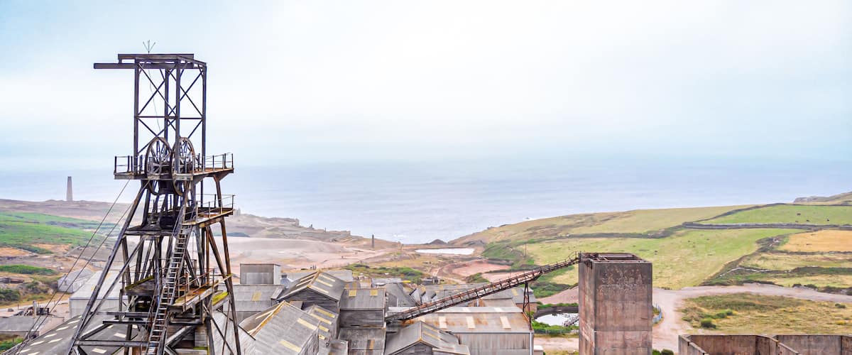 An industrial area with a conveyor belt system, large metal structures, and a coastal landscape in the background.