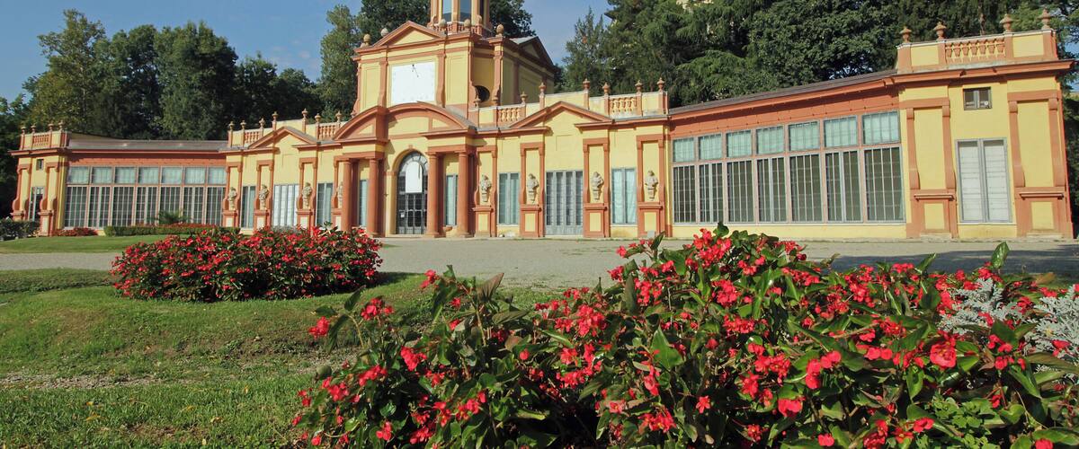 A large yellow building with a dome and columns, surrounded by green grass and red flowers.