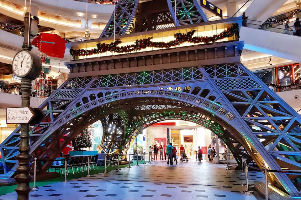 A shopping mall with a large Eiffel Tower replica, a clock, and a sign reading "Funiculaire de Montmartre".