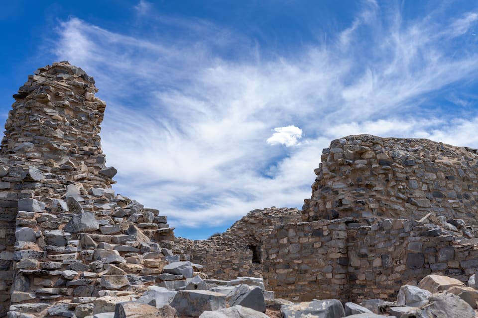 Ruinas de piedra antiguas con un cielo azul despejado y algunas nubes dispersas.