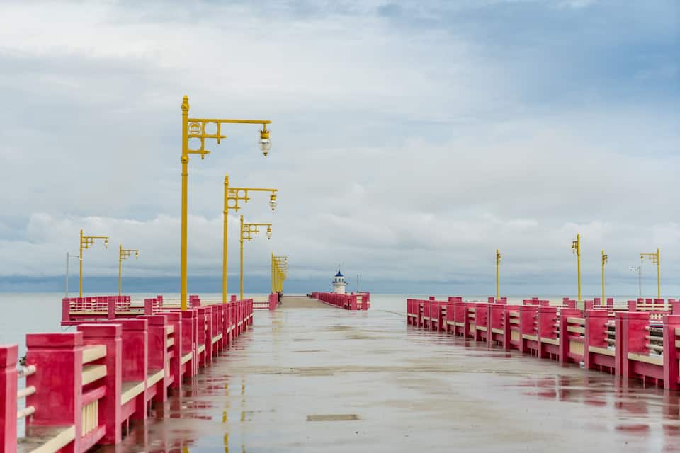 A pier with red railings and yellow street lamps extending into the water.
