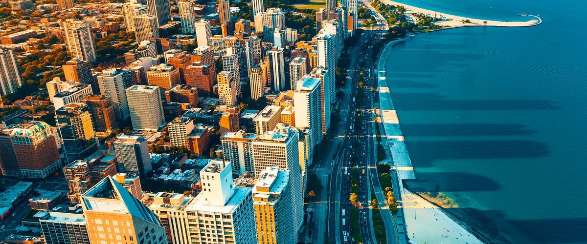 An aerial view of a coastal city with high-rise buildings, a curved waterfront promenade, and a beach.