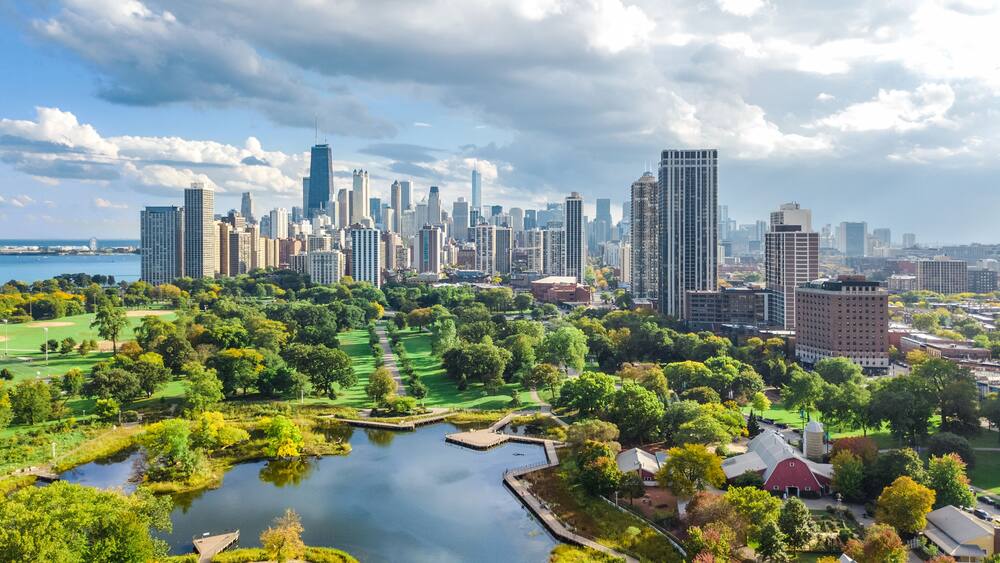 A cityscape with a large body of water, green park areas, and tall buildings.