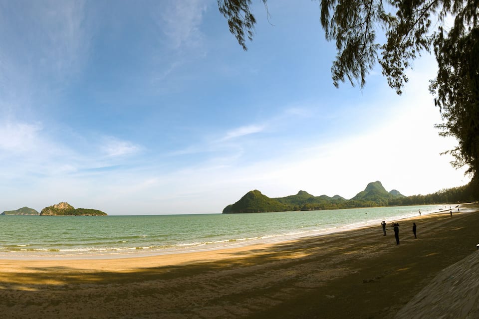 A beach with clear water, sandy shore, and distant mountains.