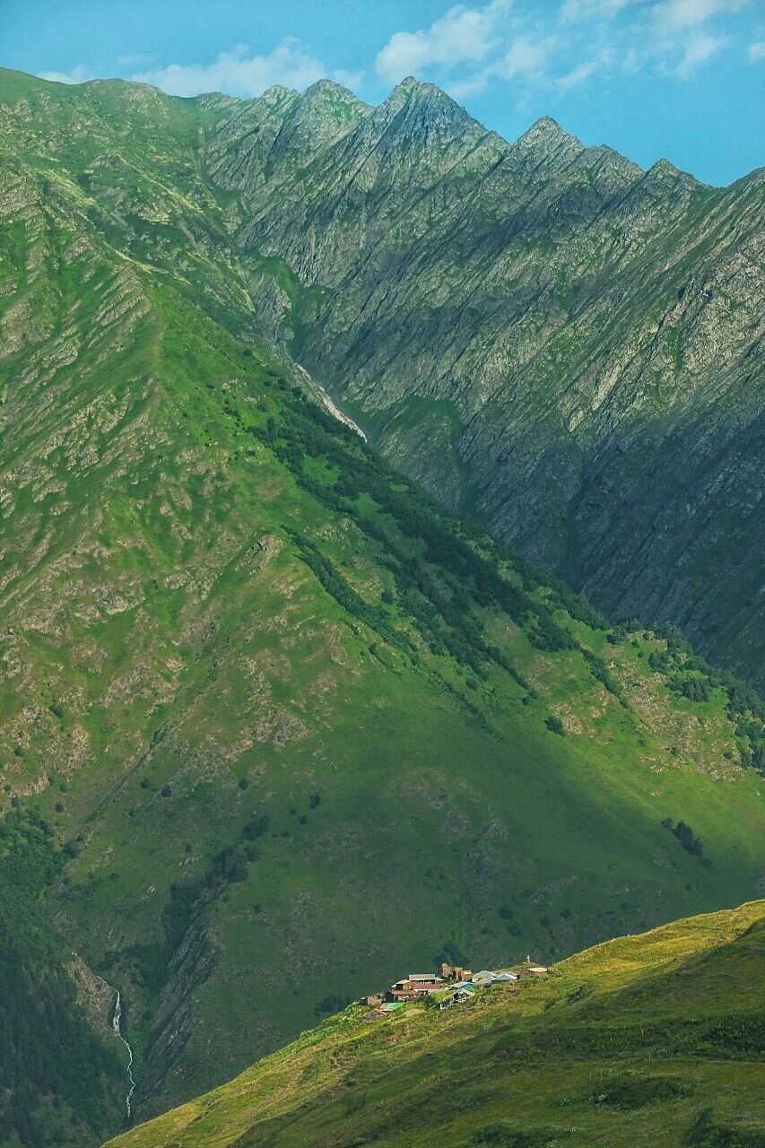Un paisaje montañoso con un valle y un pequeño asentamiento a su pie.