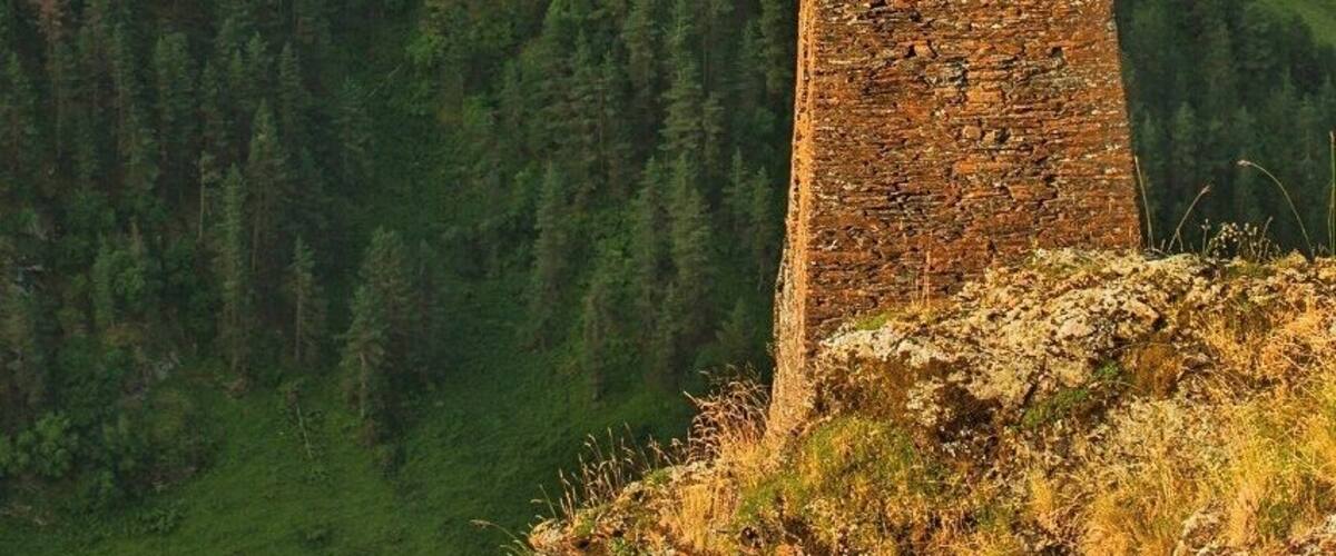 Uma torre de pedra numa encosta, com um vale florestado ao fundo.