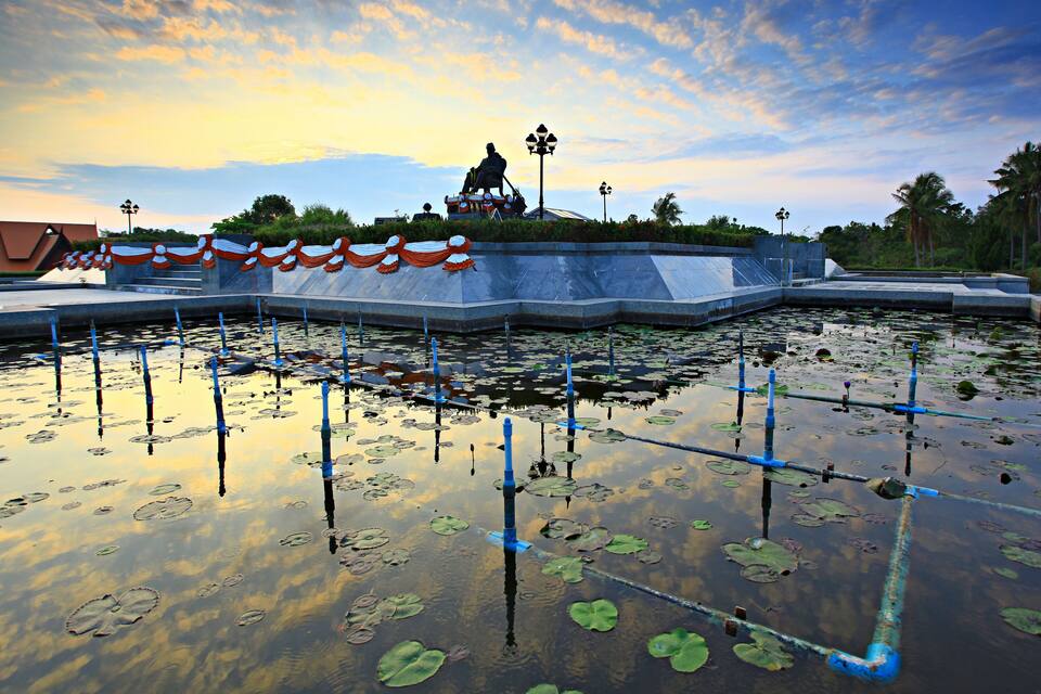 A water body with lily pads and a statue on a platform.
