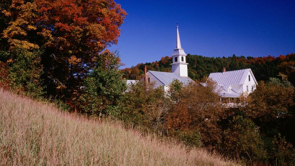 A church with a steeple surrounded by autumn foliage.