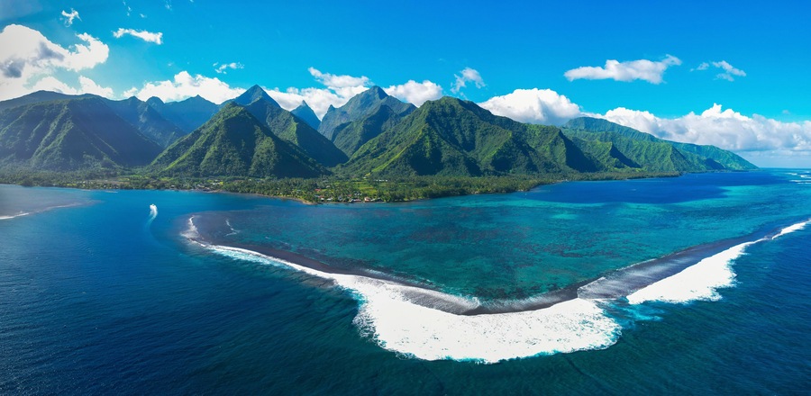 A tropical island with a clear blue sea, white sandy beaches, and lush green mountains.