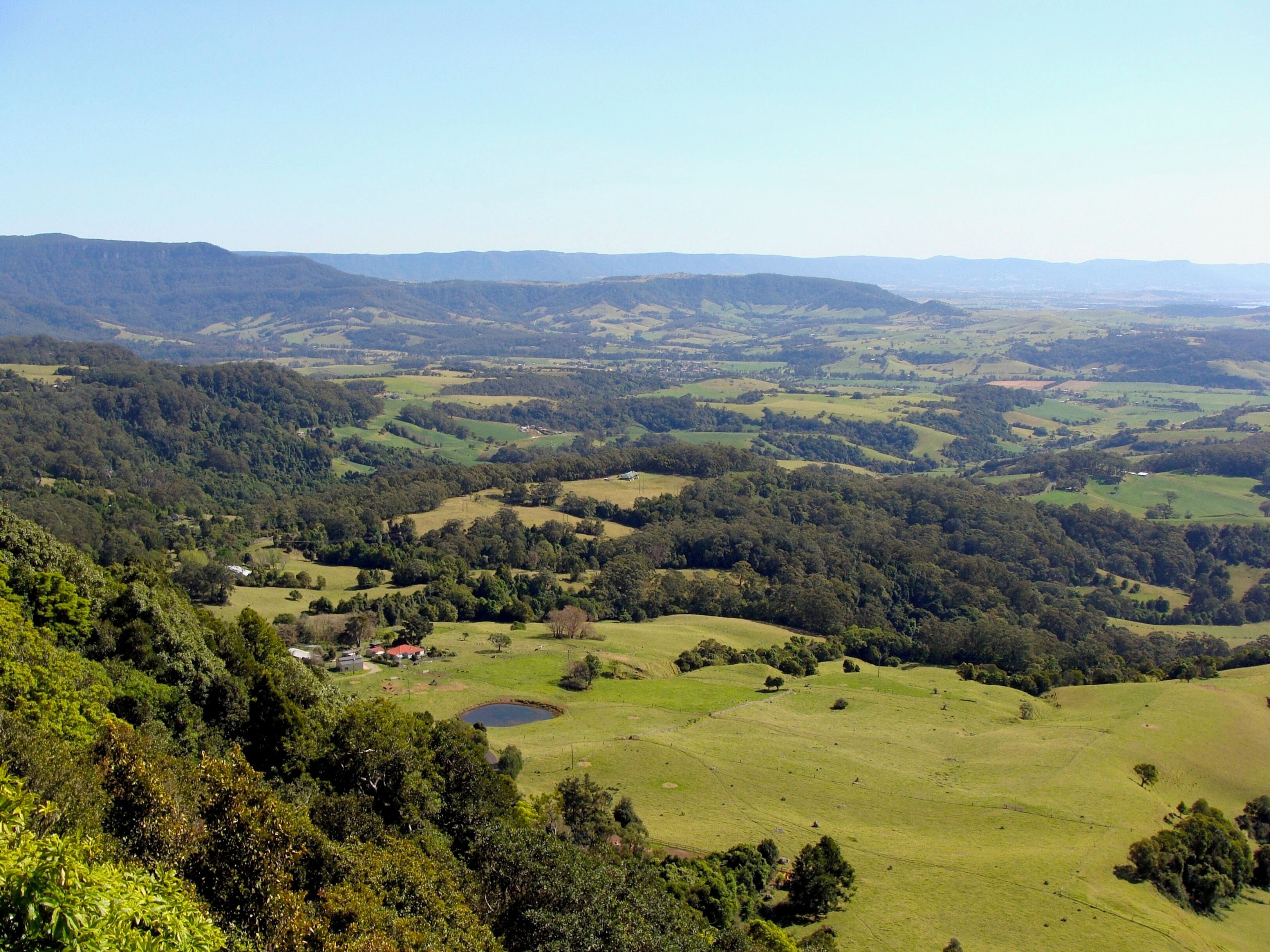A panoramic view of rolling hills, a small pond, and scattered buildings in a rural landscape.